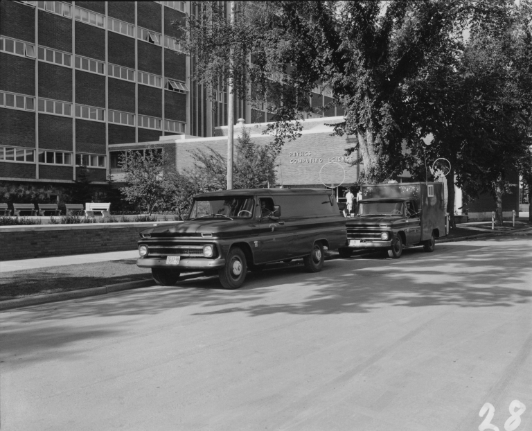 Geophysics field trucks, 1967, parked in front of the original Physics building, University of Alberta, North Campus. The Department of Computing Science, created in 1964, shared the building with the Department of Physics until 1968. The Physics Building was later renamed the Avadh Bhatia Physics Building in honor of one of its professors, then demolished to make way for the Centennial Centre for Interdisciplinary Science (which opened in 2011). The circles are radio antennas, possibly to communicate with equipment in the field. Photo Courtesy: Department of Physics, University of Alberta.